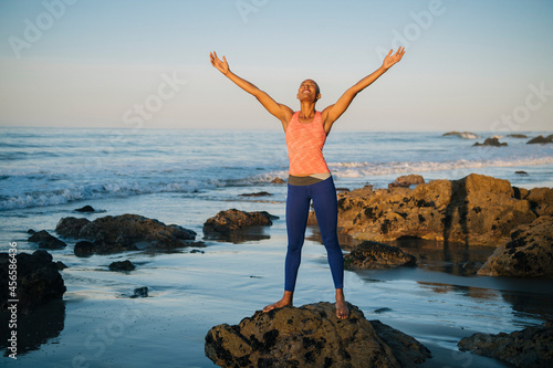 Young woman standing on rocks on beach, arms raised