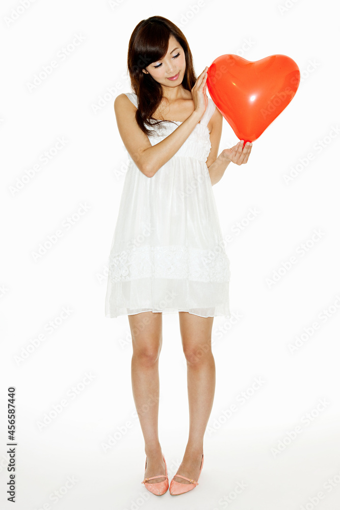 Woman holding red heart shaped balloon, studio shot Woman holding red heart shaped balloon, studio shot