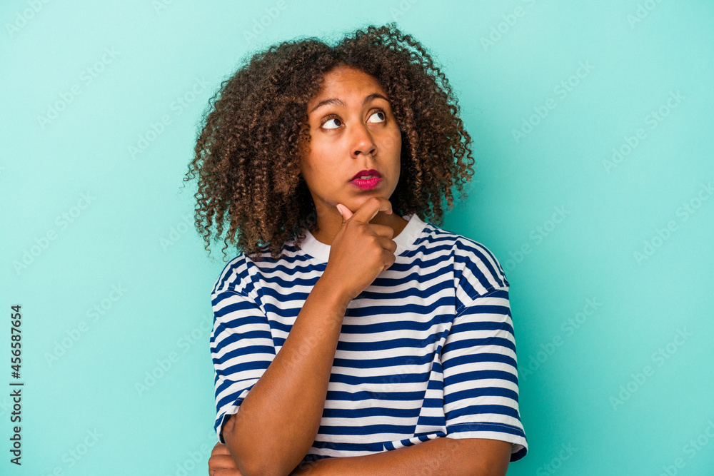 Young african american woman with curly hair isolated on blue background looking sideways with doubtful and skeptical expression. Young african american woman with curly hair isolated on blue background looking sideways with doubtful and skeptical expression.