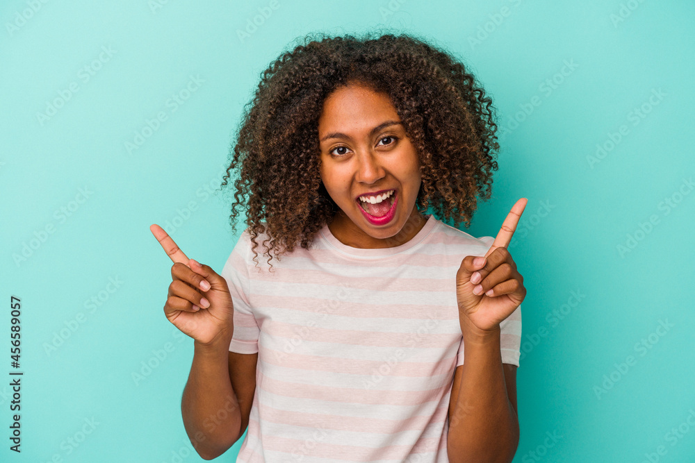 Young african american woman with curly hair isolated on blue background pointing to different copy spaces, choosing one of them, showing with finger. Young african american woman with curly hair isolated on blue background pointing to different copy spaces, choosing one of them, showing with finger.