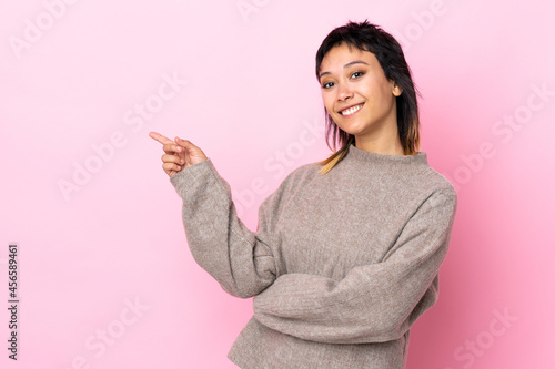 Young Uruguayan woman over isolated pink background pointing finger to the side