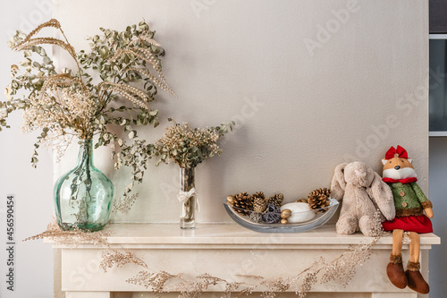 Dried plants in vases and cones with toys on fireplace photo