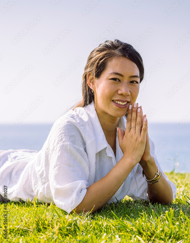 Charming Asian woman with clasped hands resting on grass shore Charming Asian woman with clasped hands resting on grass shore