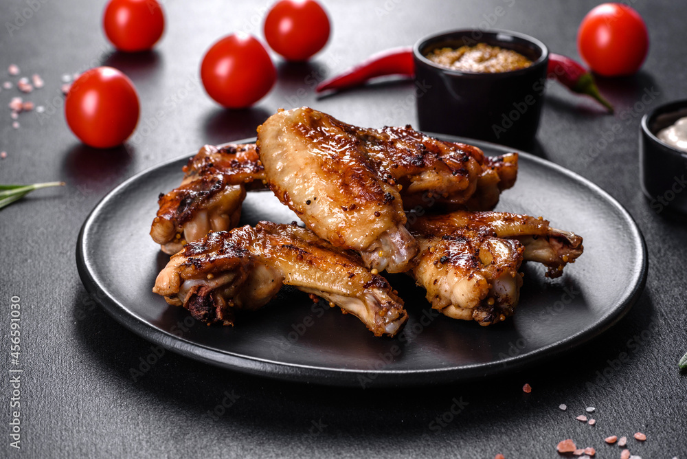 Grilled spicy chicken wings on a dark background with spices and herbs