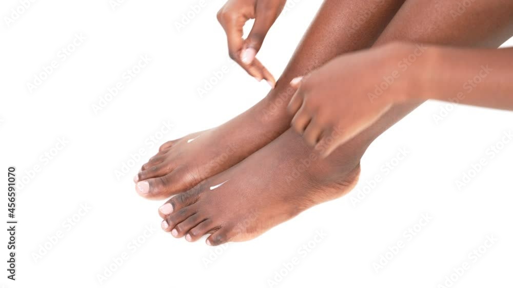 Close up of an African woman hands rubbing moisturizer lotion into the skin of her feet. White background. Close up of an African woman hands rubbing moisturizer lotion into the skin of her feet. White background.