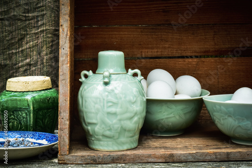 Celadon green Asian style ceramic bottle and bowls filled with white eggs inside vintage wooden box still life photo
