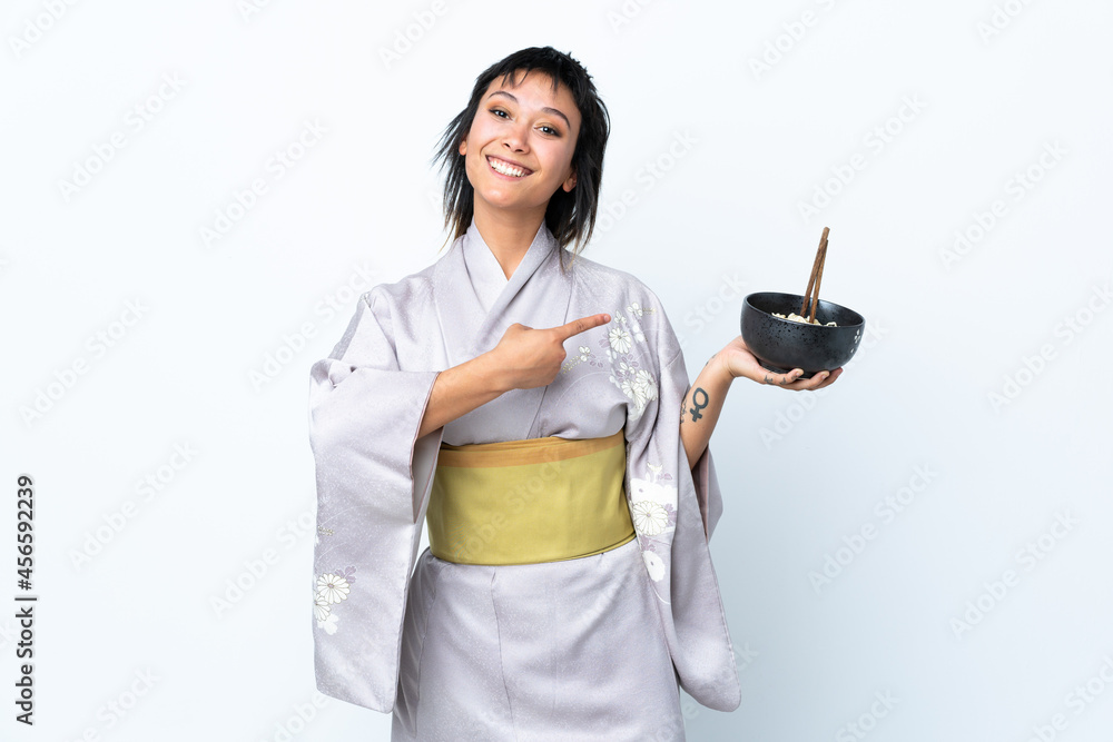 Young woman wearing kimono holding a bowl of noodles over isolated white background and pointing it Young woman wearing kimono holding a bowl of noodles over isolated white background and pointing it