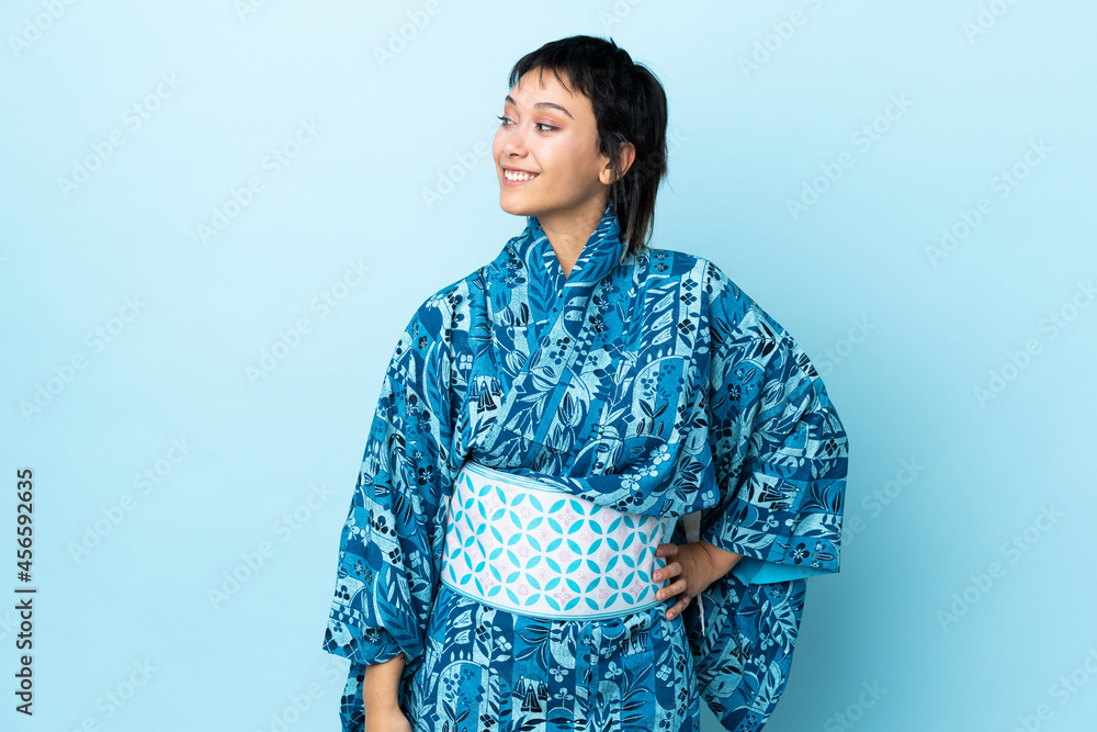 Young woman wearing kimono over isolated blue background looking to the side and smiling