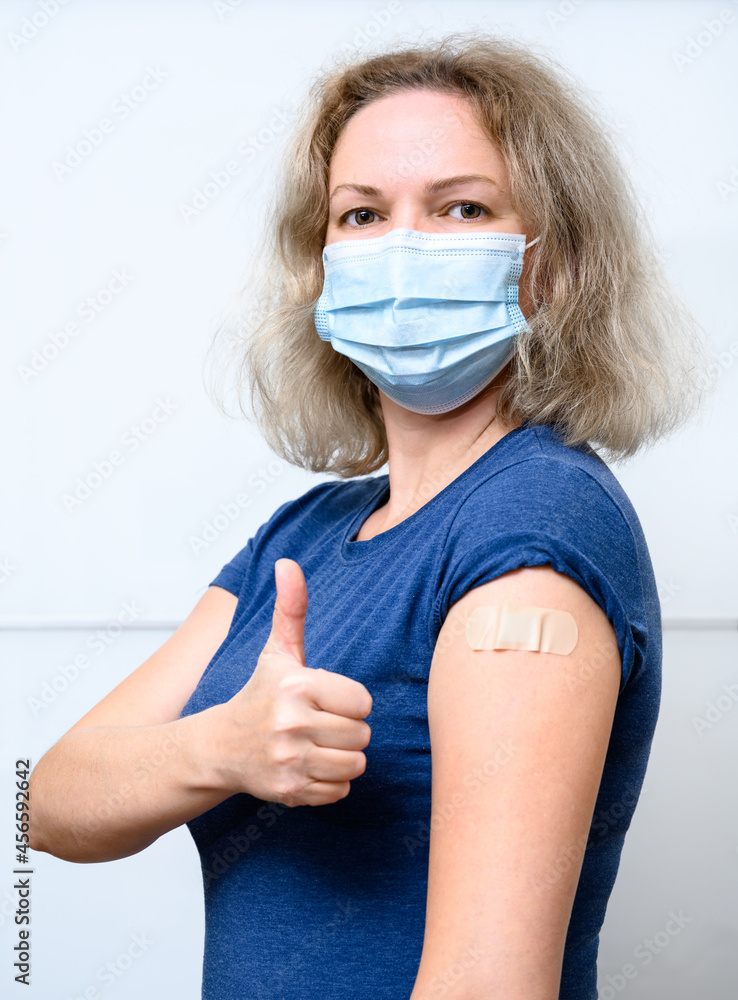 Vaccinated young woman showing shoulder with plaster. COVID-19 vaccine concept. - obrazy, fototapety, plakaty 