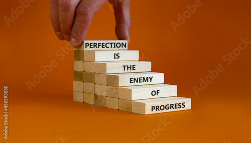Perfection or progress symbol. Wooden blocks on orange background, copy space. Businessman hand. Words 'Perfection is the enemy of progress'. Business, progress or perfection concept. Copy space. photo