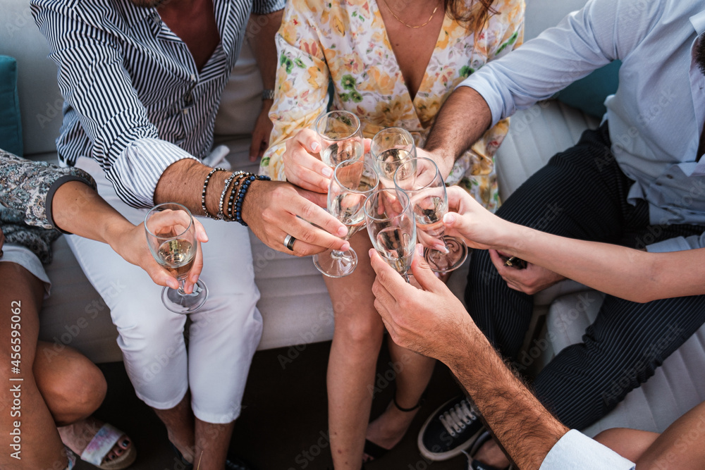 Obraz premium Group of young friends toasting sparkling white wine glasses at outdoor party - Friendship celebration with happy people enjoying time together at the terrace garden drinking champagne