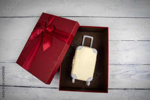 Trip as a gift concept. red gift box with miniature travel suitcase
