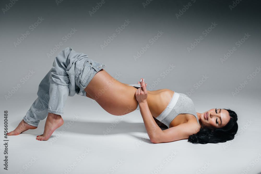 Young sexy brunette posing lying down in underwear and jeans on a gray background. The perfect athletic figure. Young sexy brunette posing lying down in underwear and jeans on a gray background. The perfect athletic figure.