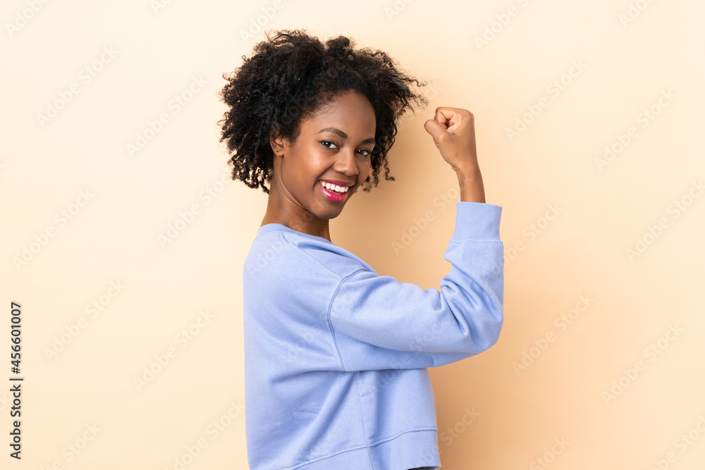 Young African American woman isolated on beige background doing strong gesture Young African American woman isolated on beige background doing strong gesture