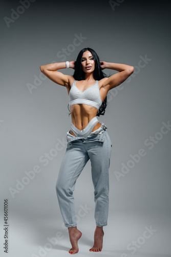 Young sexy brunette posing in lingerie and jeans on a gray background. The perfect athletic figure.