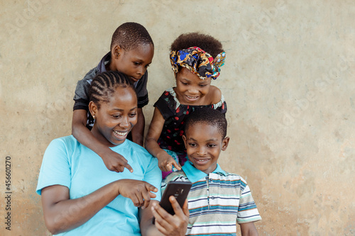 African single mother and her children smiling while using a smartphone