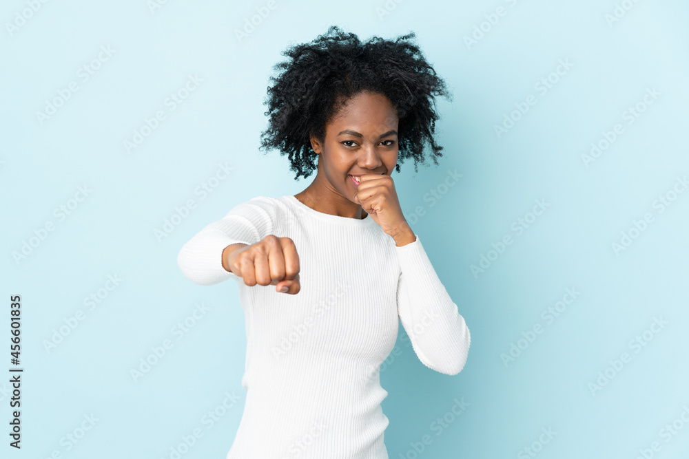 Young African American woman isolated on blue background with fighting gesture Young African American woman isolated on blue background with fighting gesture