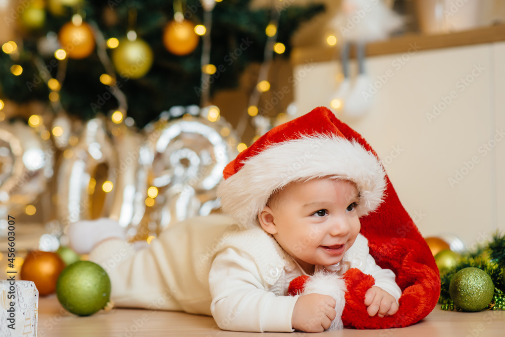 Cute smiling baby is lying under a festive Christmas tree and playing with gifts. Christmas and New Year celebrations Cute smiling baby is lying under a festive Christmas tree and playing with gifts. Christmas and New Year celebrations