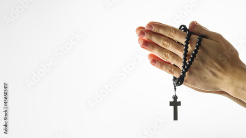 Rosary and crucifix in female hands on a white background. Hands folded for prayer. Religion, Catholicism, prayer, faith, meditation. There is an empty space for insertion. Minimalism.
