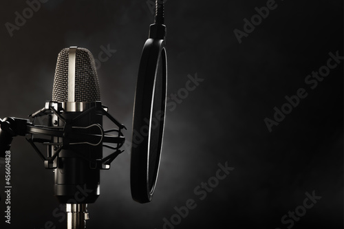 Professional studio microphone and pop filter. Dark gray background. Minimalism. Recording studio, vocals, conversational genre, radio broadcasting, music, clear sound.