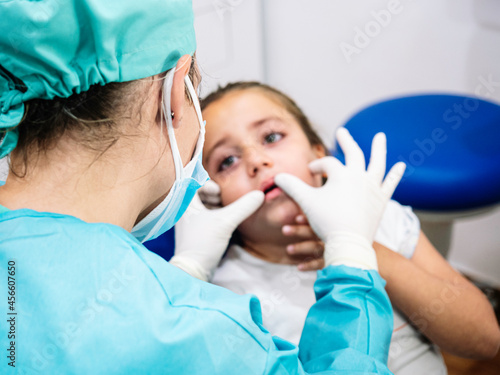 Caucasian girl looking with concern at an unrecognizable dentist giving her a check-up in her office. Concept of oral health.