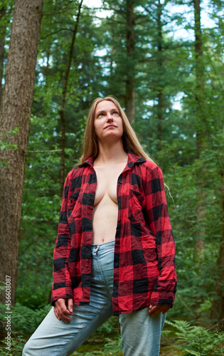 A Caucasian female standing in the forest with her shirt unbuttoned © Érik Glez.