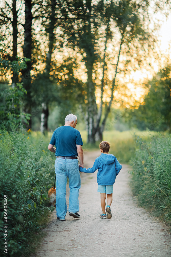 Fototapeta premium Grandfather walks with his grandson and dog in the park