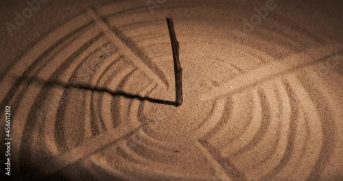 Stylized as a sundial. Rod, sunbeam and circles in the sand.