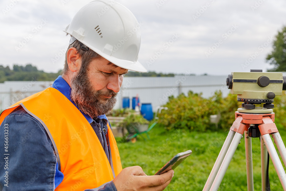A civil engineer with an optical level looks into a mobile phone. A civil engineer with an optical level looks into a mobile phone.