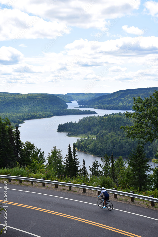 Mauricie National Park, Quebec, Canada: View of Lake Wapizagonke and a cyclist on the road from the passage viewpoint (Belvédère du passage) Mauricie National Park, Quebec, Canada: View of Lake Wapizagonke and a cyclist on the road from the passage viewpoint (Belvédère du passage)