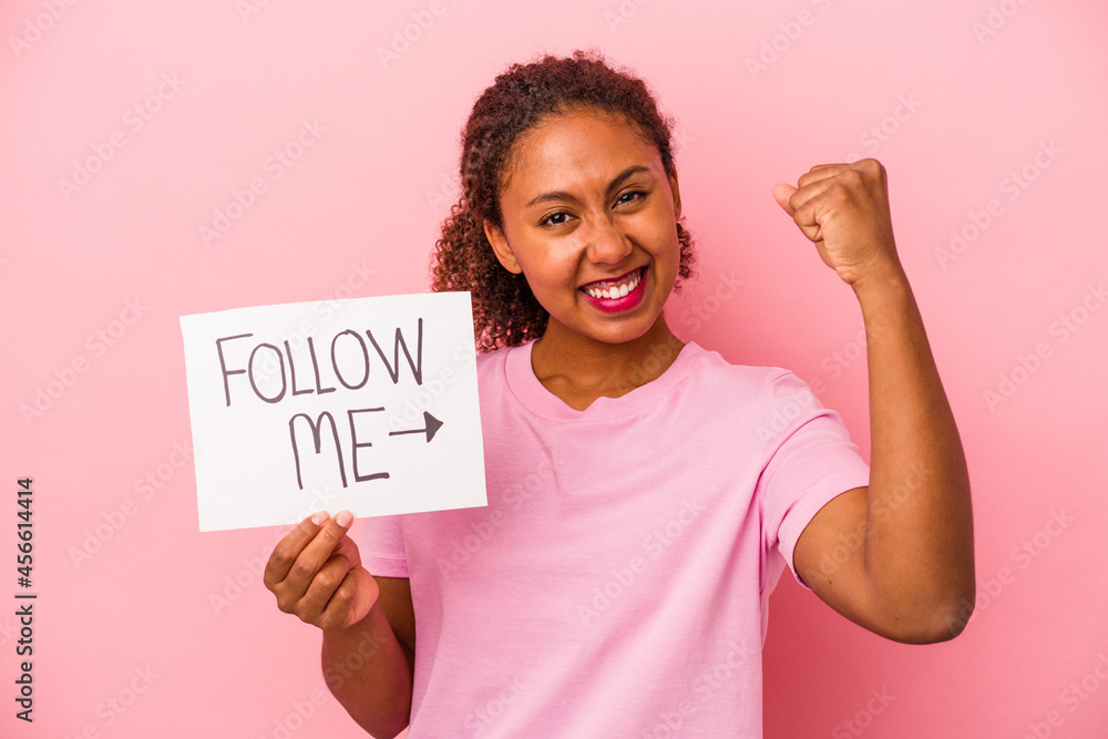 Young African American woman holding a follow me placard isolated on pink background Young African American woman holding a follow me placard isolated on pink background