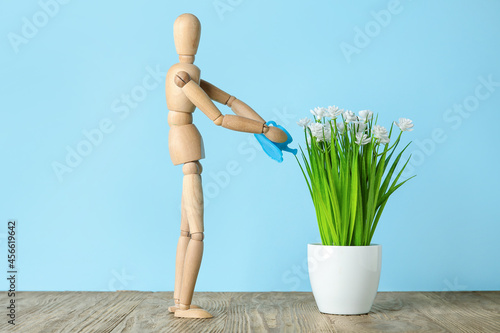 Wooden mannequin watering plant on color background. Concept of gardening