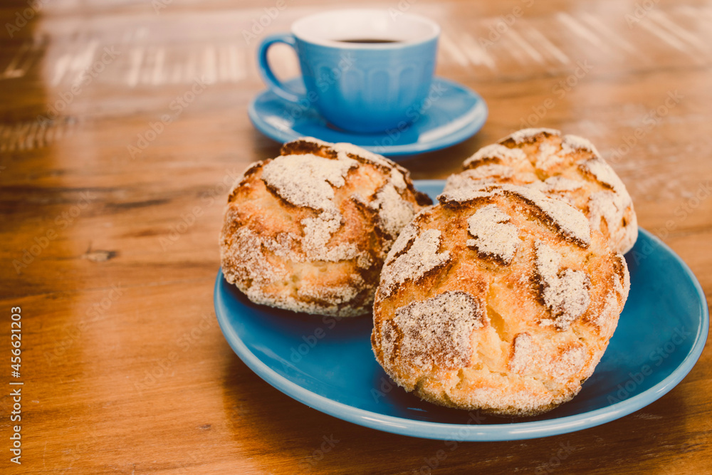 A cup of coffee and three brazilian corn breads on the table. 