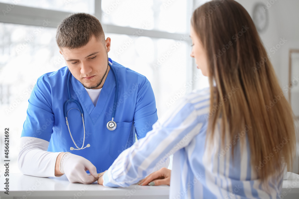 Doctor applying plaster onto hand of young woman in clinic Doctor applying plaster onto hand of young woman in clinic