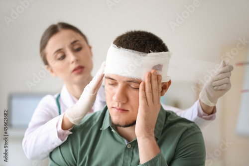 Doctor applying bandage onto head of young man in clinic photo