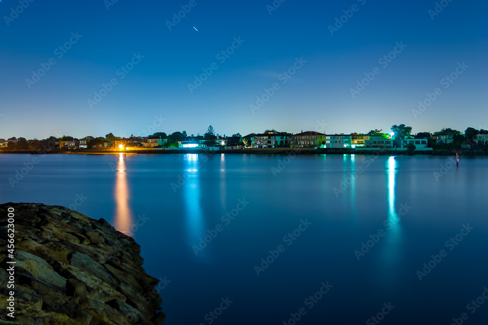 Long exposure of coastal town at night with lights reflecting in the blurry water