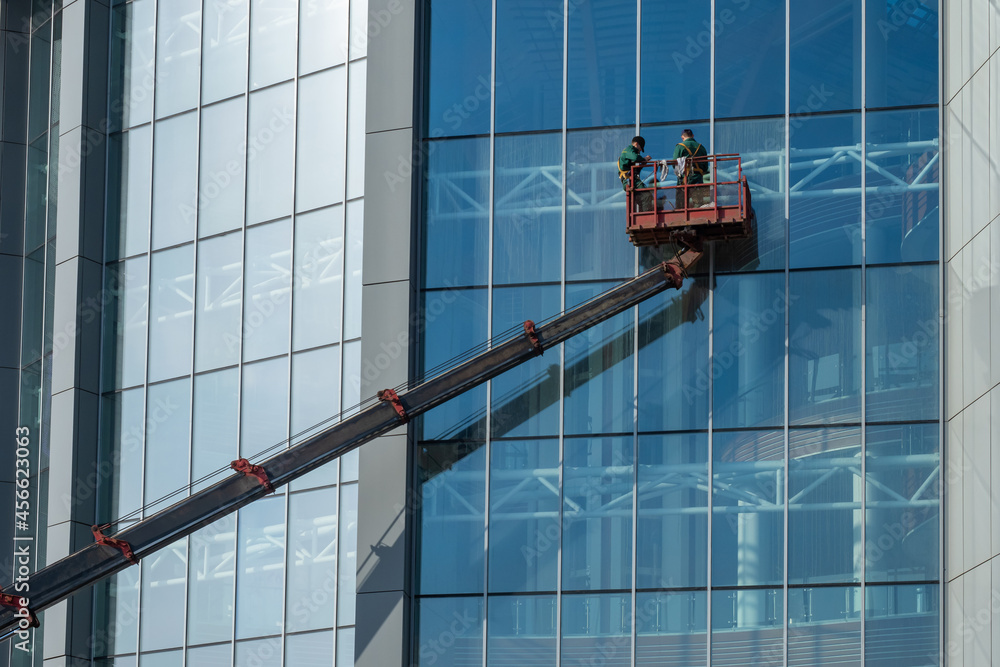 Workers are washing walls of building. Two men on boom of tower crane