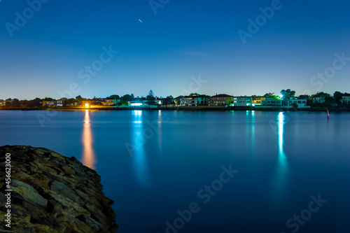 Long exposure of coastal town at night with lights reflecting in the blurry water