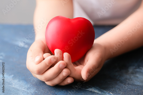 Child holding red heart on color background  closeup. Cardiology concept