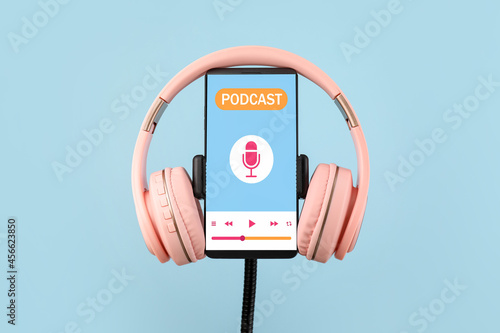 Obraz na płótnie Modern headphones and mobile phone with podcast playlist on screen against color