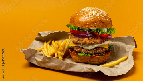 Big breaded chicken burger with double cutlet and fries on craft paper. Fat unhealthy street food. Copy space photo