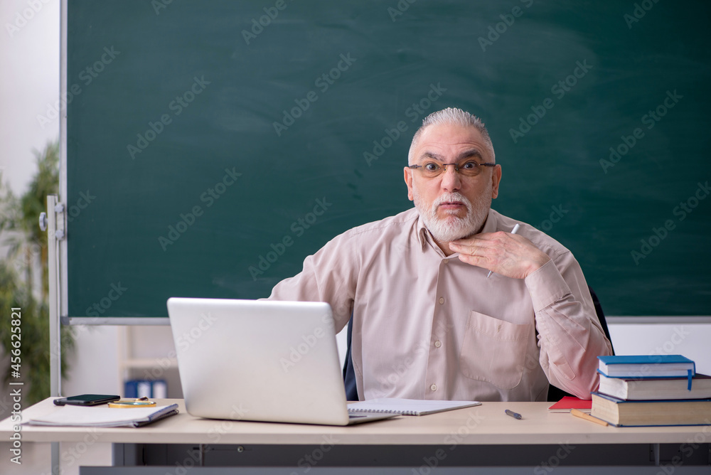 Old male teacher in front of blackboard Old male teacher in front of blackboard