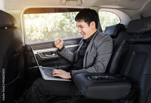 successful business man using laptop computer while sitting in the back seat of car