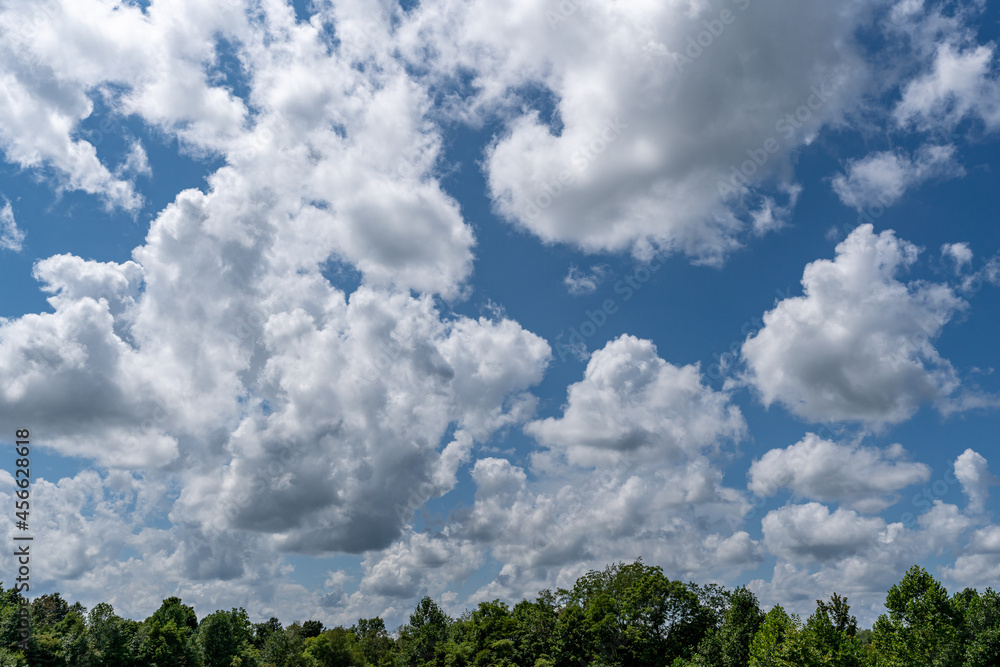 White cotton like puffy cumulus clouds against a blue sky with the suns rays shining. White cotton like puffy cumulus clouds against a blue sky with the suns rays shining.