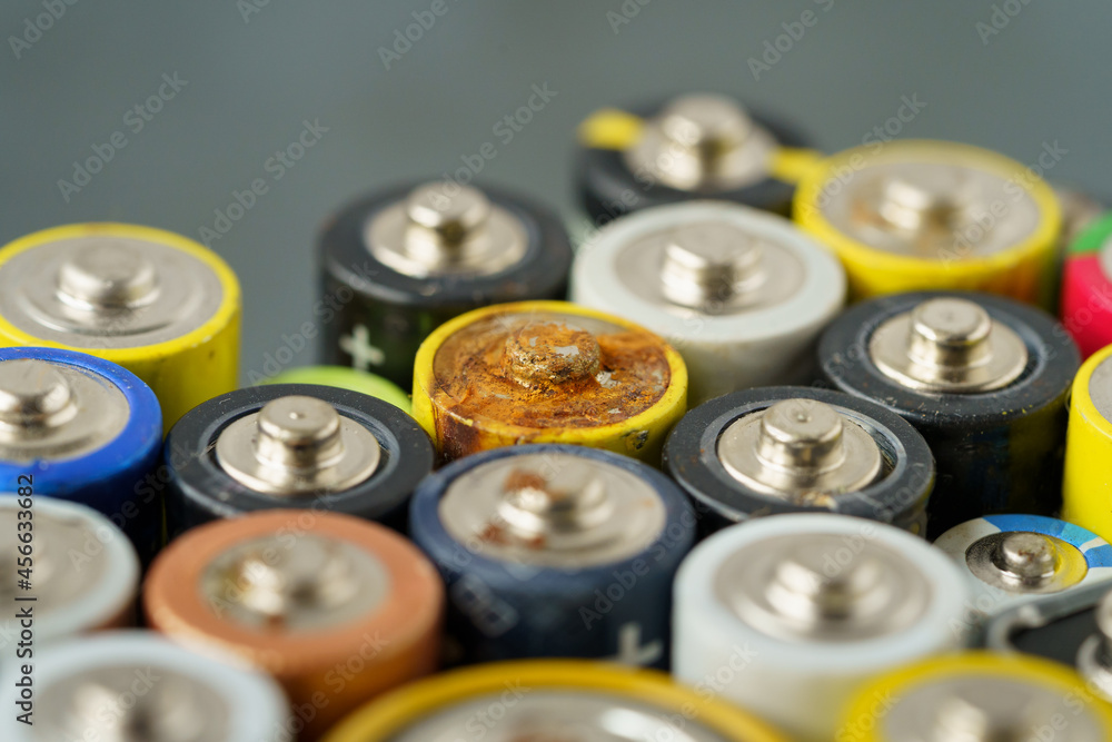 Close up of used battery with traces of rust and corrosion, selective soft focus. Lot of AA batteries over grey background. Electronic hazardous waste, recycling concept Close up of used battery with traces of rust and corrosion, selective soft focus. Lot of AA batteries over grey background. Electronic hazardous waste, recycling concept