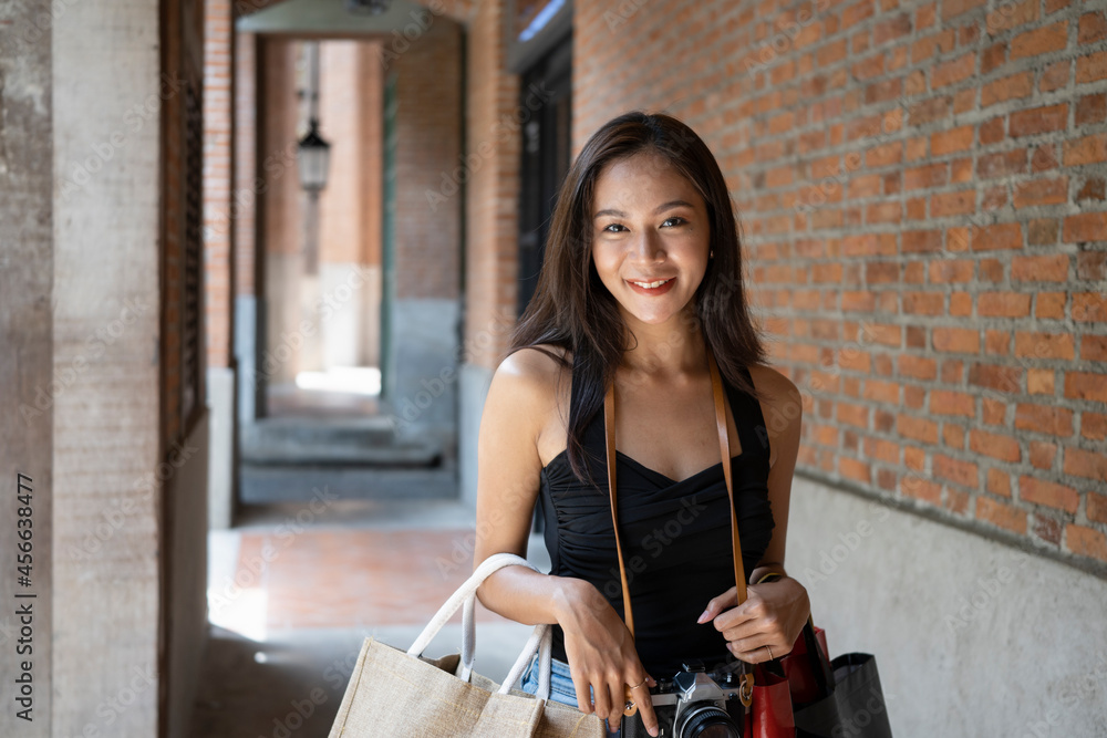 Young Asian woman traveler holding her shopping bags and smiling to camera.