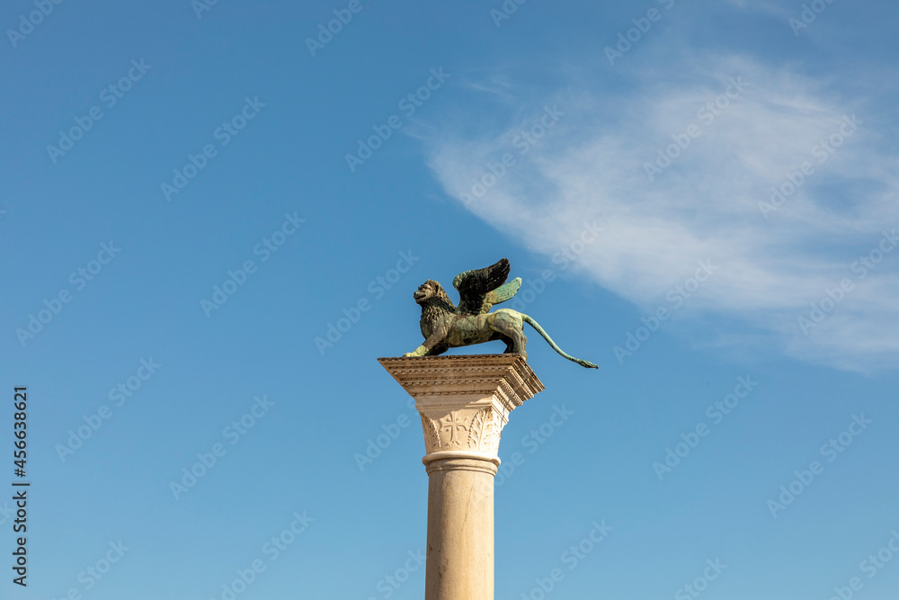 Bronze lion on the Piazza San Marco on blue sky background, Venice, Italy. Winged lion is a symbol of Venice. Ancient statue on a pillar close-up in Venice center