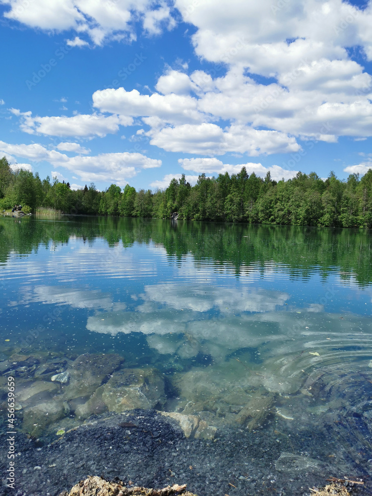 The shore of the lake is bright with clear water, in which you can see the marble on the bottom and reflect the sky with clouds, in the mountain park Ruskeala.