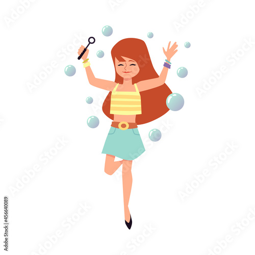 Cute child girl with red hair having fun playing with flying soap bubbles.