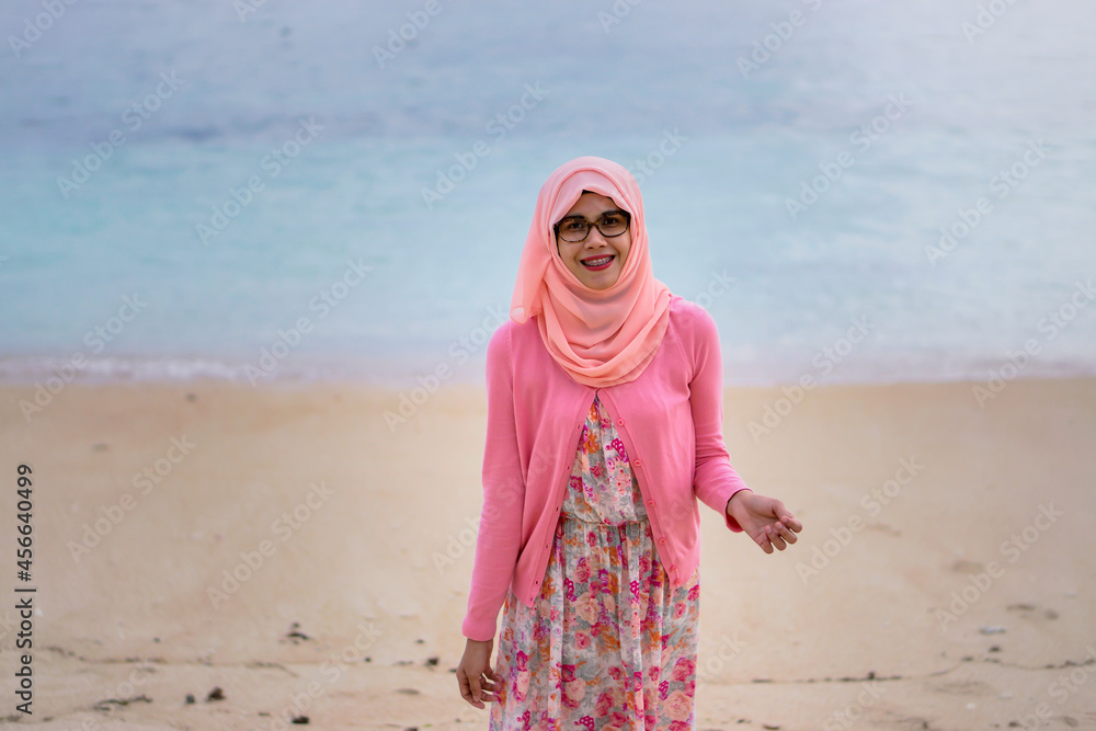 Φωτογραφία Portrait of beautiful young Asian muslim woman wearing pink dress and hijab standing by tropical beach looking at camera